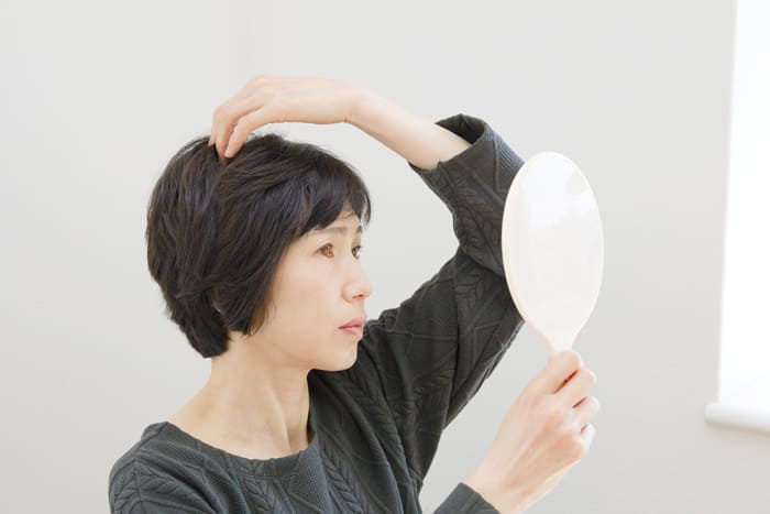鏡を見て薄毛を確認する女性